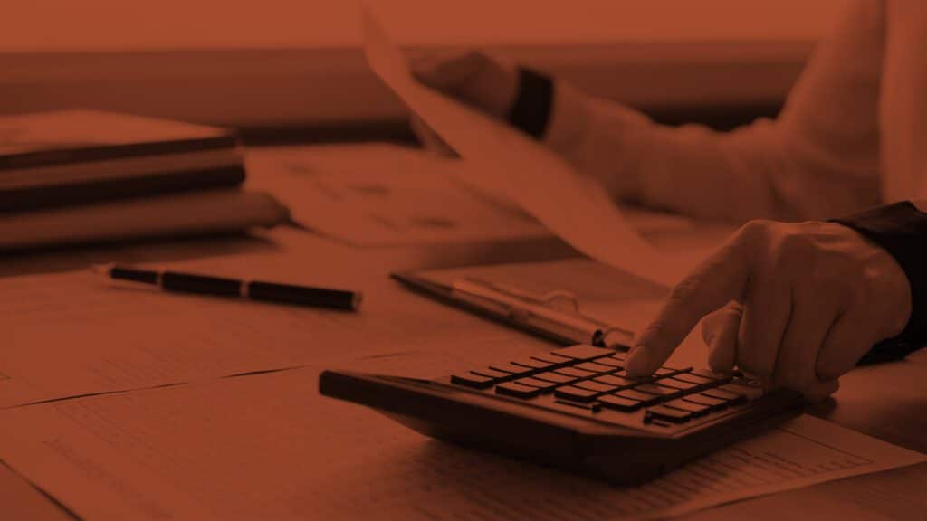 Is Search Marketing More Effective Than Traditional Advertising? Feature Image: Person at Desk Looking at Spreadsheets and Working a Calculator